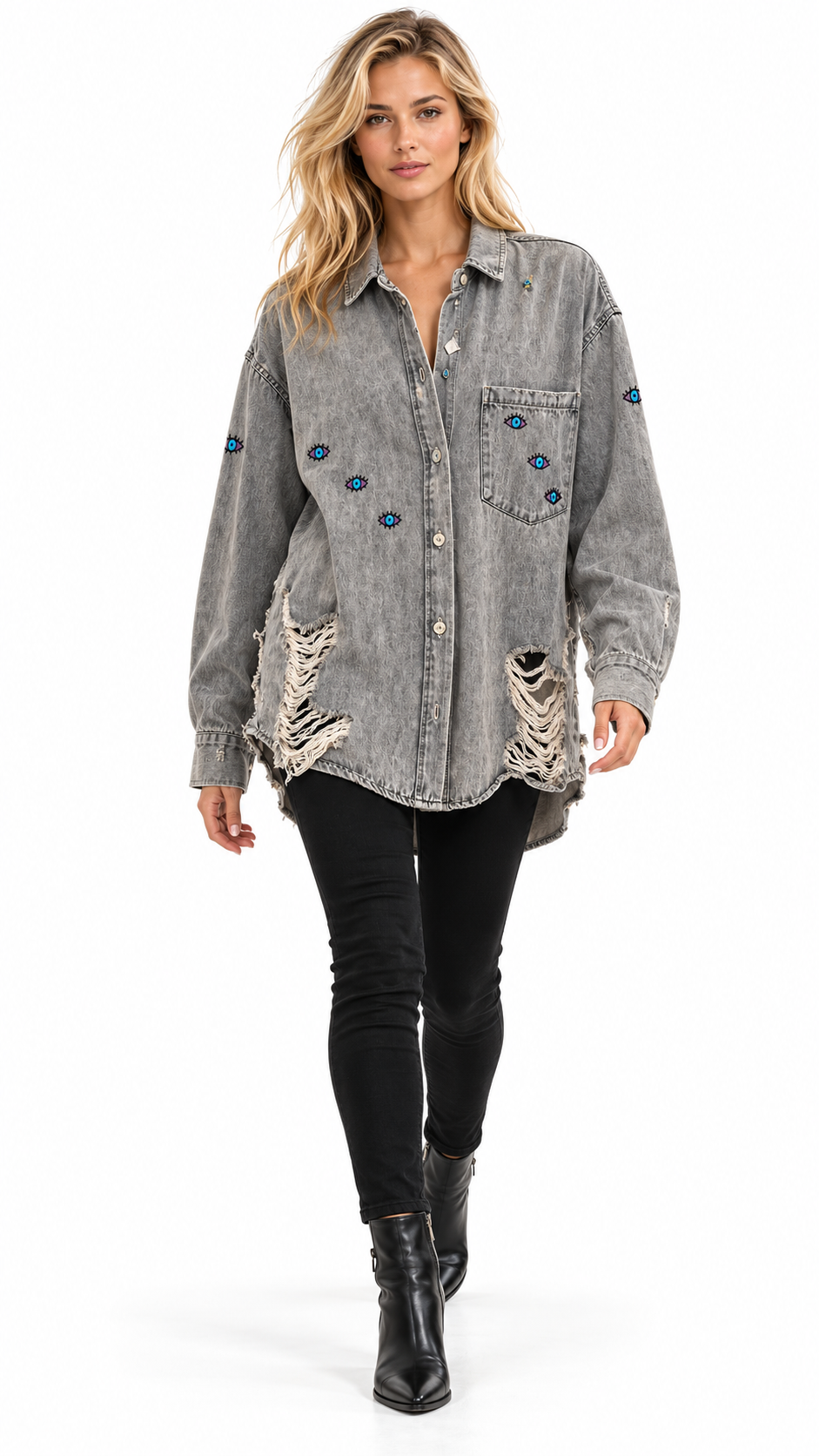 A woman modeling a gray acid-wash denim shirt jacket with blue embroidered details and distressed rips, paired with black skinny pants and black ankle boots on a white studio background.