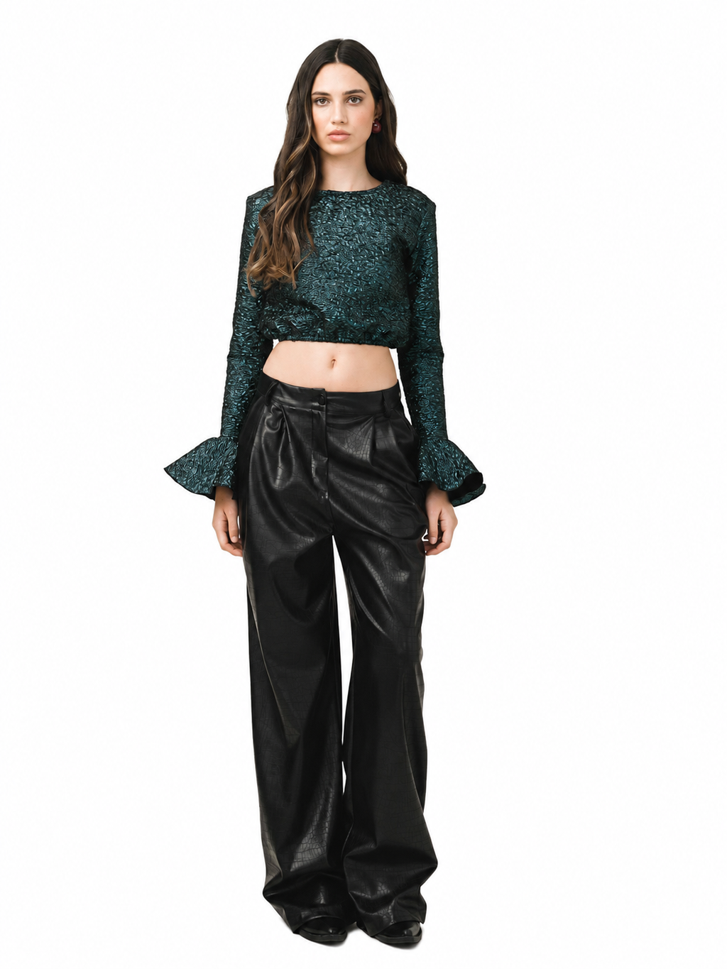 A model stands against a white background wearing a dark green textured long-sleeve crop top with flared cuffs and black wide-leg faux-leather pants.
