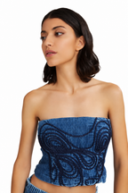 A woman wearing a blue strapless tube top with dark blue embroidered swirl patterns, photographed against a plain white background.