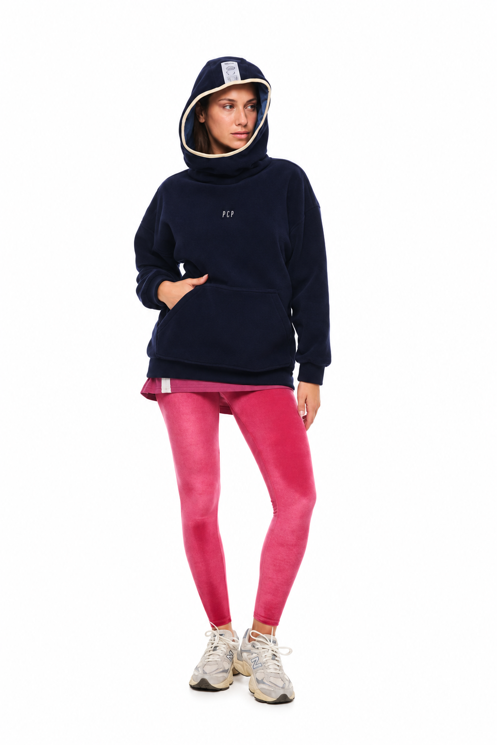 A model wearing a navy blue fleece hoodie with a white embroidered logo, paired with bright pink leggings and white sneakers, standing against a solid white background.
