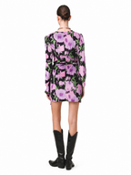 A model viewed from the back wearing a long-sleeve mini dress with a pink and purple floral print on a black background, paired with black knee-high boots, against a plain white studio background.
