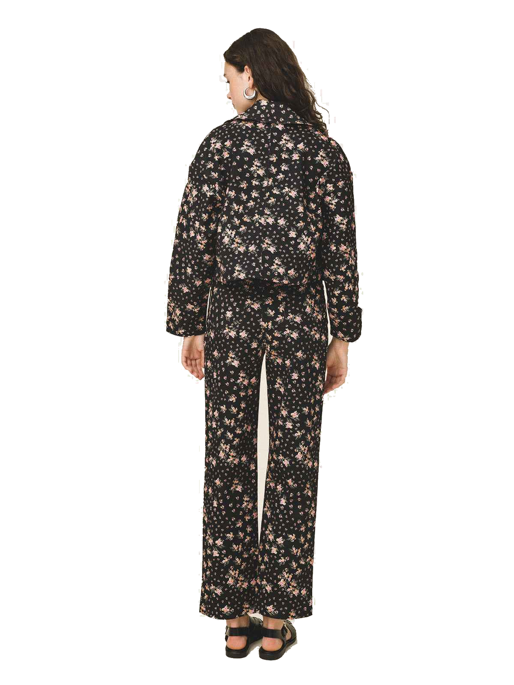 A woman viewed from the back wearing a matching long-sleeve top and wide-leg pants set in black with a small beige floral print, paired with black sandals, against a plain white background.