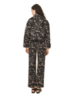 A woman viewed from the back wearing a matching long-sleeve top and wide-leg pants set in black with a small beige floral print, paired with black sandals, against a plain white background.