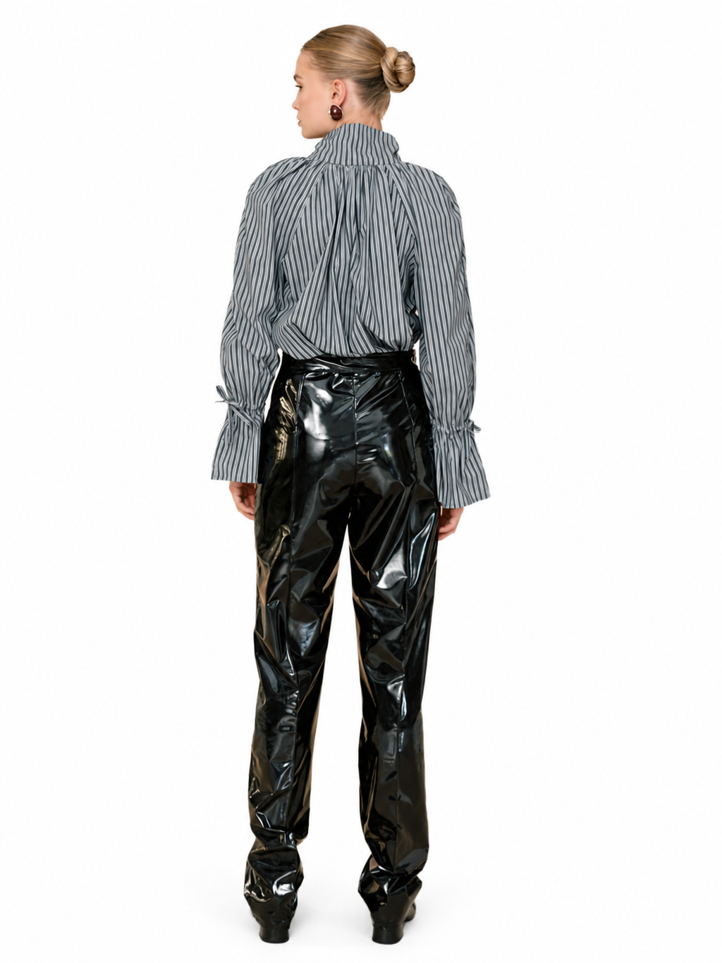 A model shown from the back wearing a gray and white vertically striped long-sleeve blouse with gathered cuffs and high-waisted, highly glossy black patent pants, set against a plain white background.