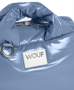 Close-up of a glossy light blue puffer-style bag with a white rectangular patch reading WOUF and a silver zipper pull.