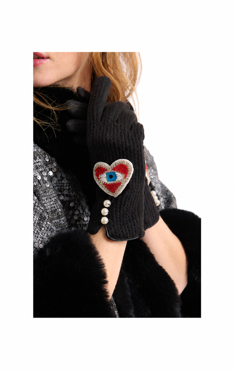 A close-up of a person wearing black knit gloves, featuring one glove with a decorative embroidered heart patch in red, white, and blue, accented with small white pearl-like beads.