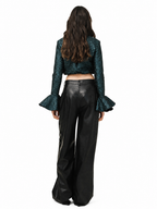 A model viewed from behind wearing a dark teal-green sequined long-sleeve crop top with flared ruffle sleeves and black wide-leg faux-leather pants, set against a plain white background.