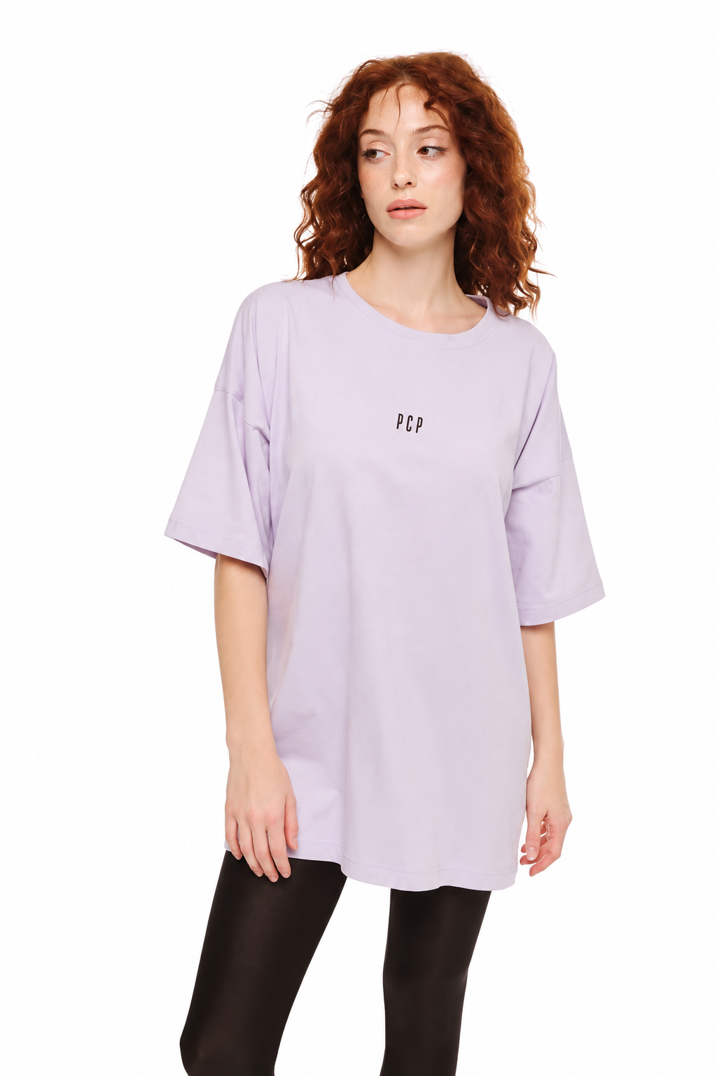 A woman with curly red hair wearing an oversized light purple t-shirt with a small black 'PCP' logo on the chest, paired with black leggings, against a plain white background.