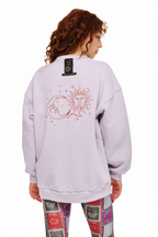 A model shown from the back wearing a light lavender crewneck sweatshirt with a large sun and moon graphic on the back, paired with patterned leggings, against a plain white background.