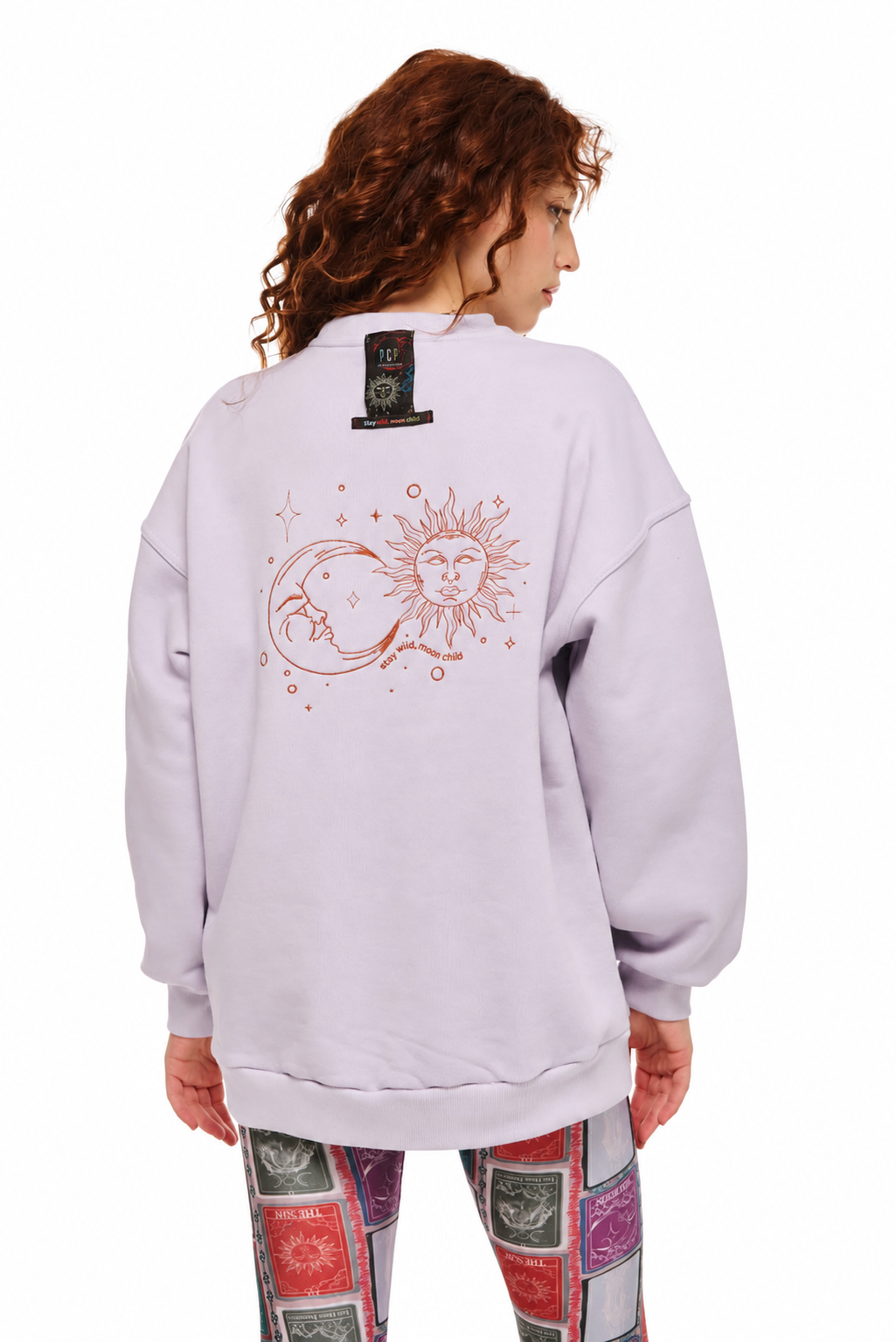 A model shown from the back wearing a light lavender crewneck sweatshirt with a large sun and moon graphic on the back, paired with patterned leggings, against a plain white background.