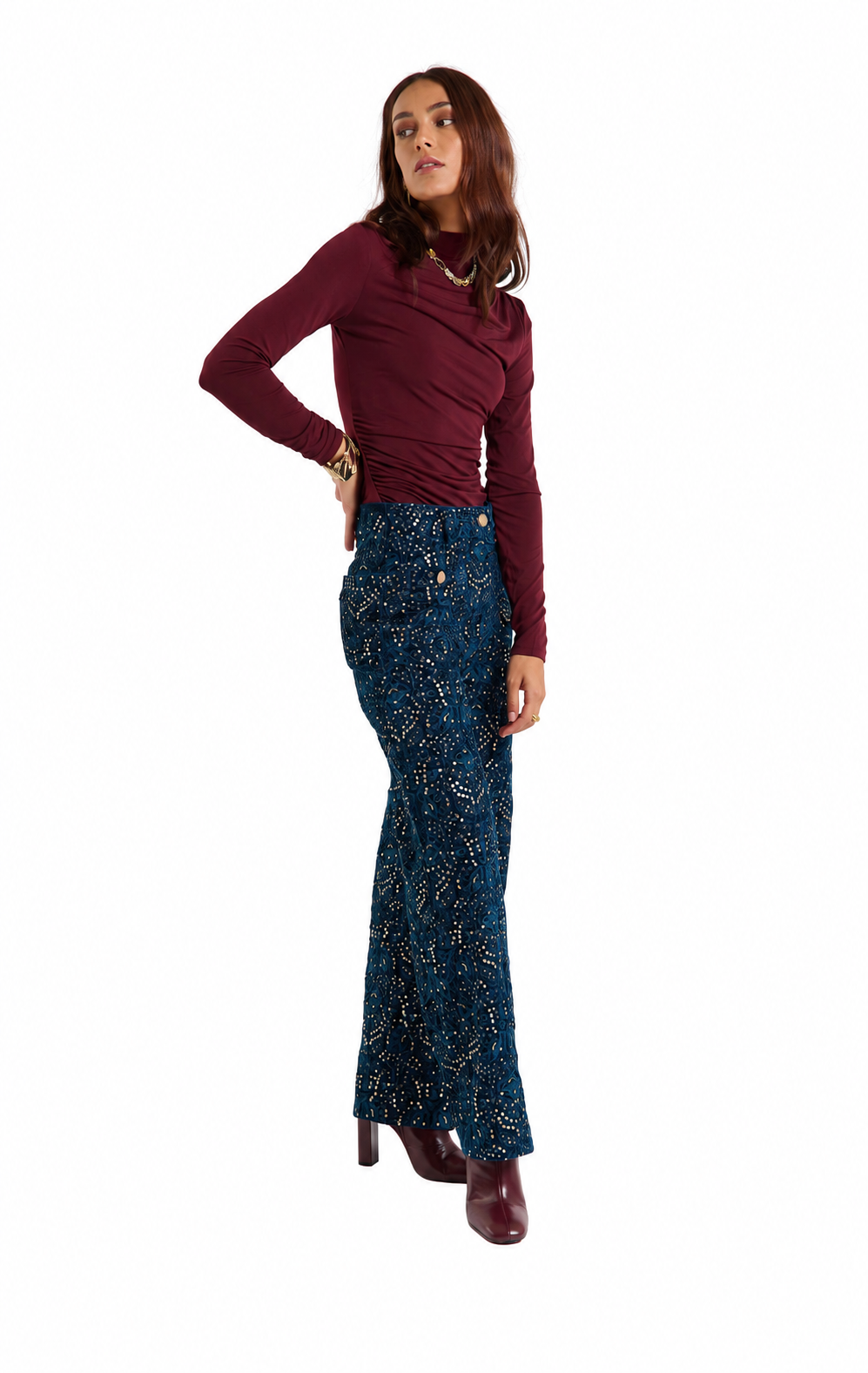 A woman modeling a dark burgundy long-sleeve wrap top and a dark blue patterned maxi skirt with gold sequins, paired with burgundy high heels, against a solid white background.