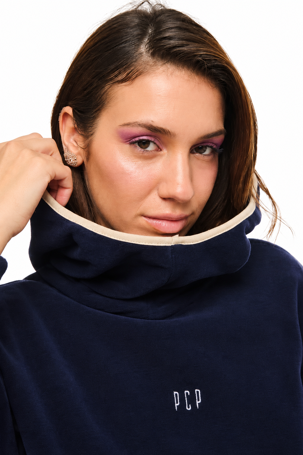 A close-up of a woman wearing a navy blue high-neck fleece pullover sweatshirt with a cream-colored inner collar trim and a small white 'PCP' logo on the chest.