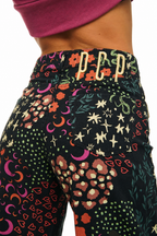 Close-up of a person wearing patterned high-waisted leggings with a black base and colorful celestial and floral motifs, featuring a gold 'PP' logo on the waistband.