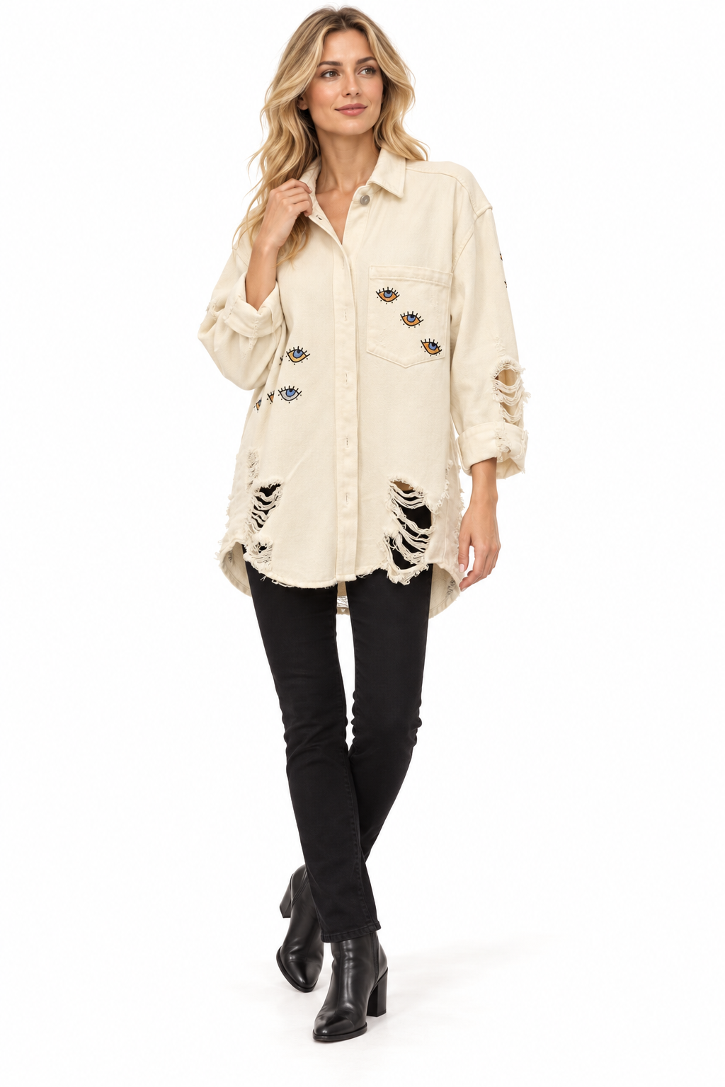 A woman modeling a distressed off-white button-up shirt with ripped details and embroidered patches, paired with black skinny jeans and black ankle boots, on a solid white background.
