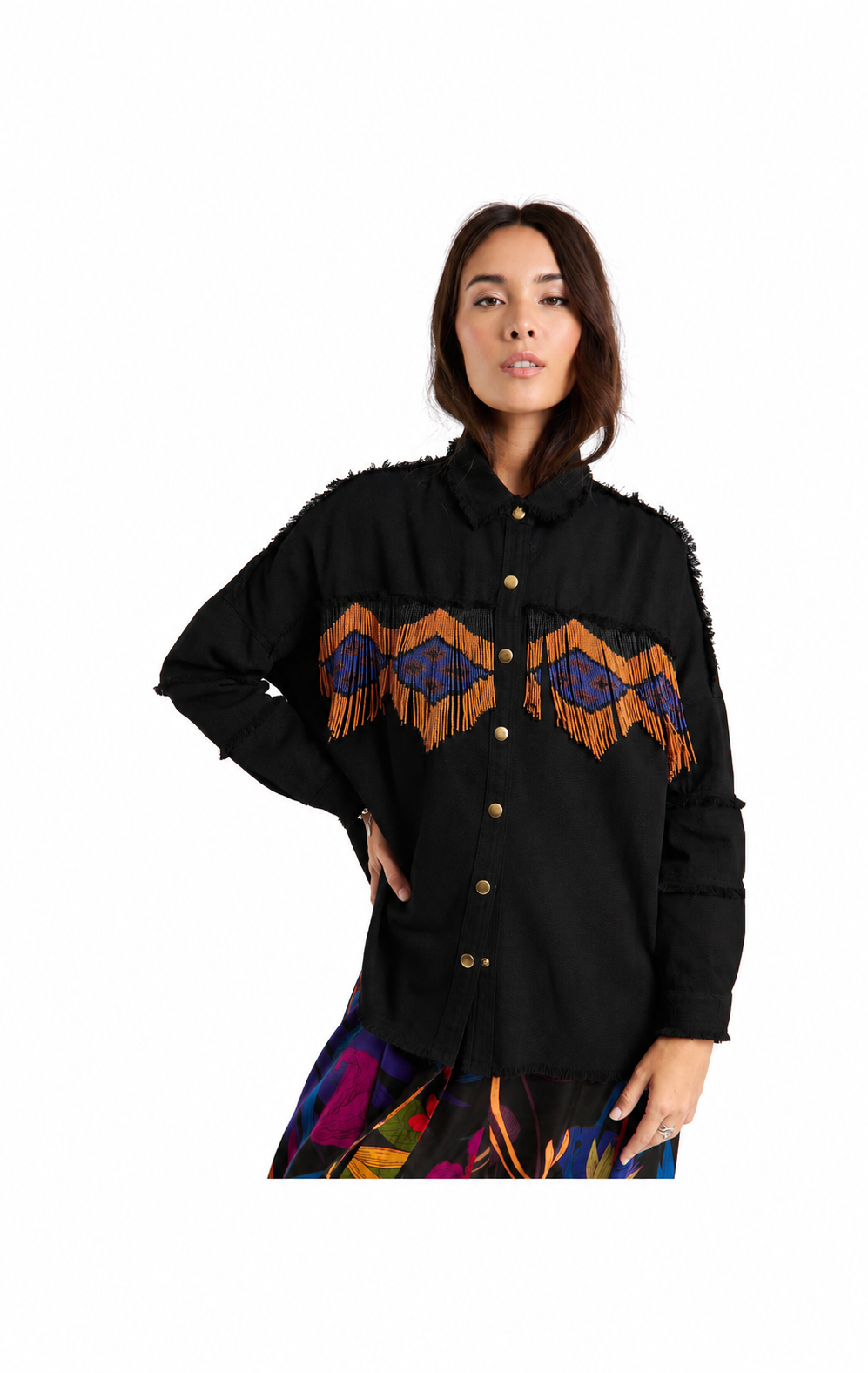 A woman modeling a black long-sleeve button-up shirt with colorful geometric embroidery and fringe details across the chest, paired with a multicolored skirt, against a plain white background.