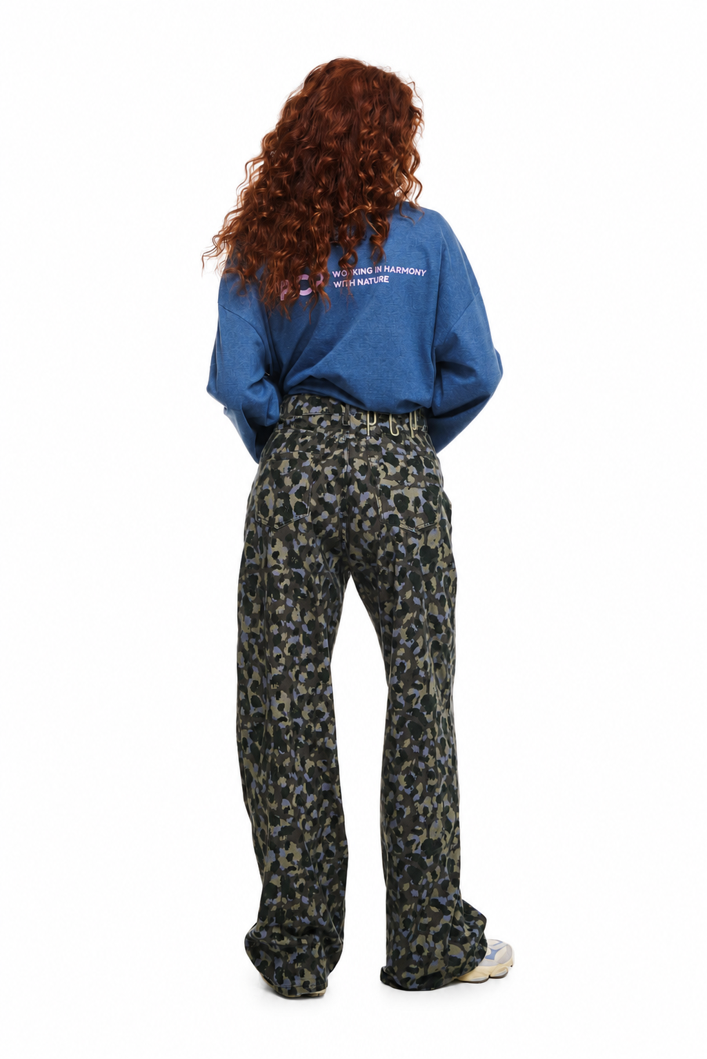 A person shown from the back wearing a blue sweatshirt and high-waisted wide-leg trousers with a dark olive, black, and tan leopard print. The photo is shot against a solid white background.