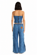 A model shown from the back wearing a matching blue denim set consisting of a strapless cropped top and wide-leg pants, photographed against a solid white background.