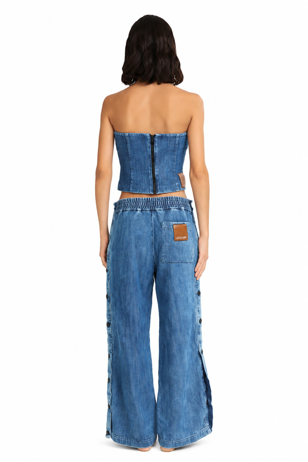 A model shown from the back wearing a matching blue denim set consisting of a strapless cropped top and wide-leg pants, photographed against a solid white background.
