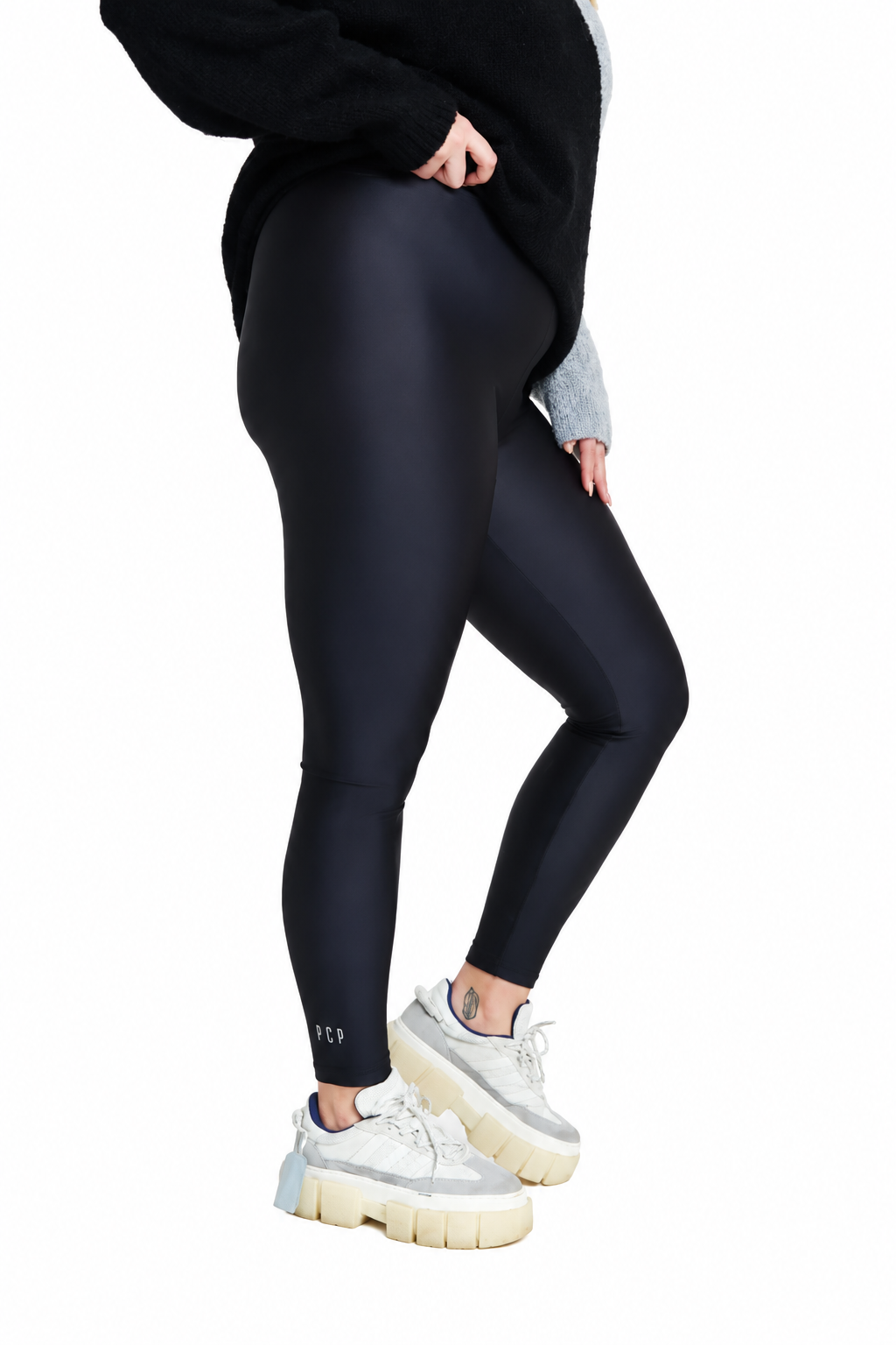 A model wearing black high-waisted leggings, a black sweatshirt, and white chunky platform sneakers, shown from the waist down against a solid white background.
