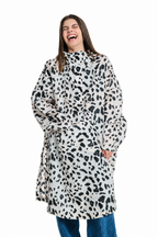 A woman laughing while wearing a high-neck, long-sleeved coat with an oversized black and white dalmatian-style animal print, paired with blue jeans, against a solid white background.