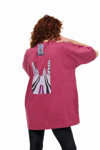 A woman viewed from behind wearing an oversized pink t-shirt with a large graphic print of a zebra on the back, paired with black leggings, against a plain white background.