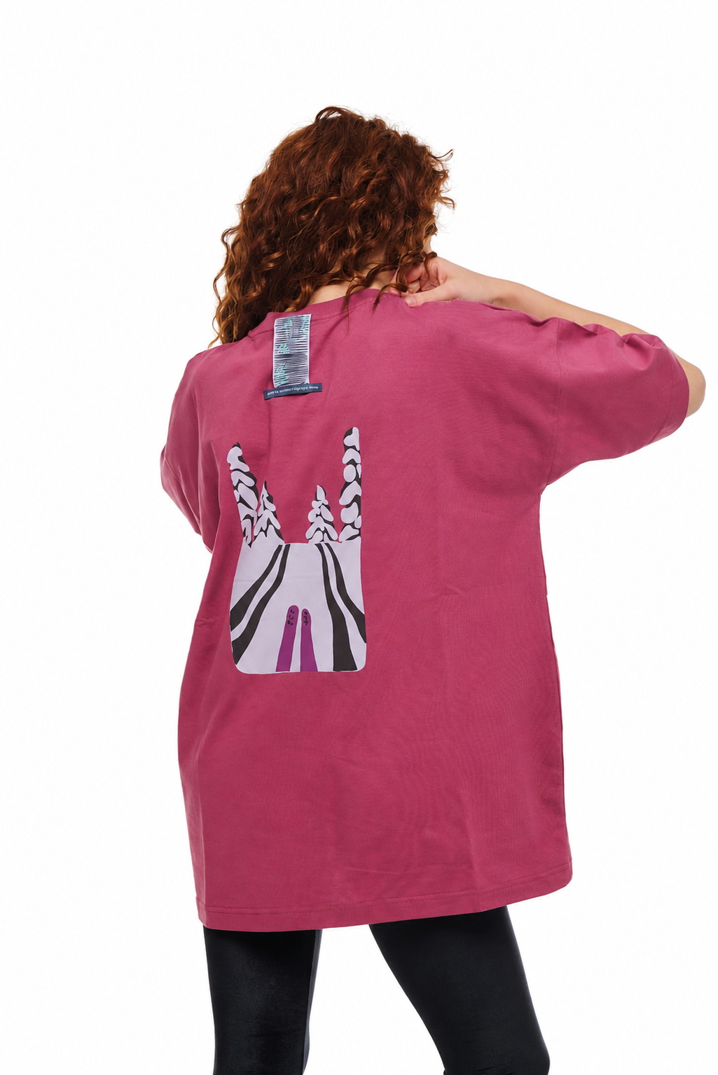 A woman viewed from behind wearing an oversized pink t-shirt with a large graphic print of a zebra on the back, paired with black leggings, against a plain white background.