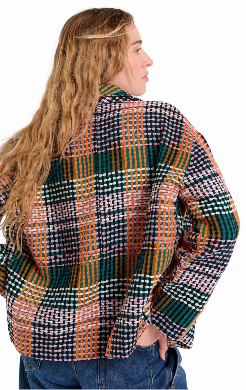 A woman shown from the back wearing a long-sleeve plaid button-up shirt with a multicolor pattern of green, orange, white, and black, paired with blue jeans against a white background.