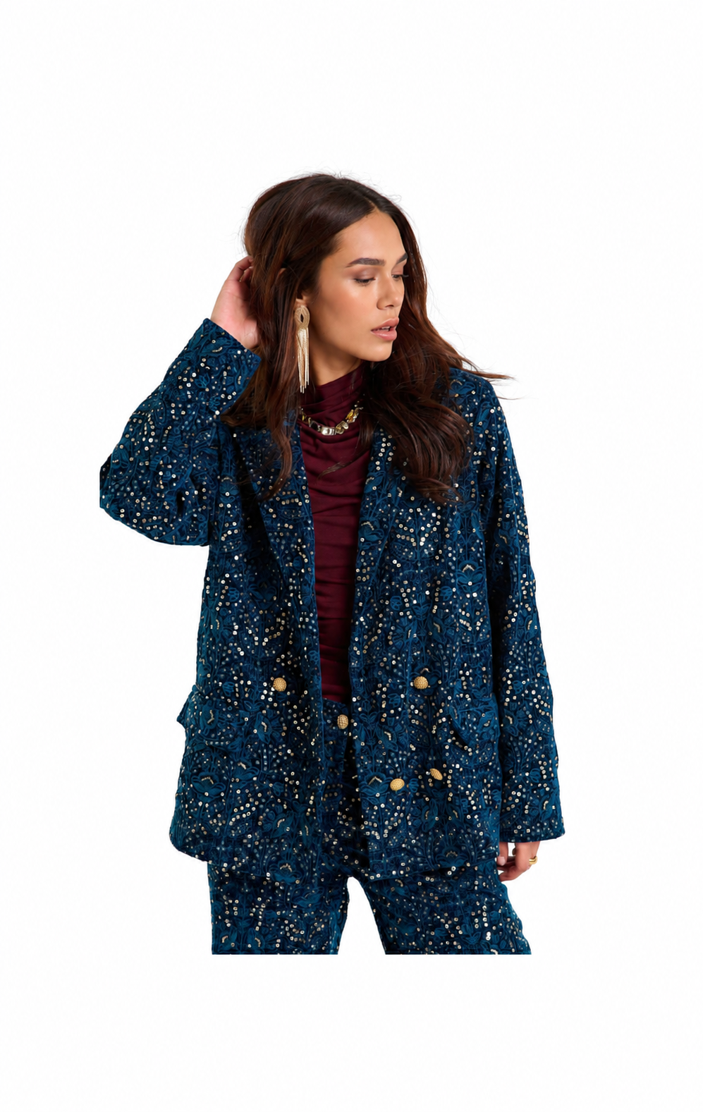 A woman modeling a dark blue sequined blazer and matching pants set with gold buttons, worn over a burgundy top, against a plain white background.