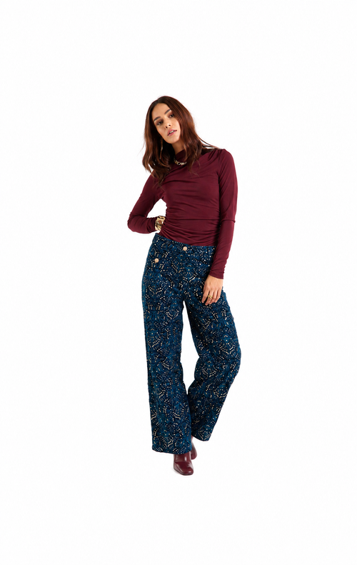 A woman modeling a dark blue patterned wide-leg trouser set with a burgundy long-sleeve top, standing against a solid white background.