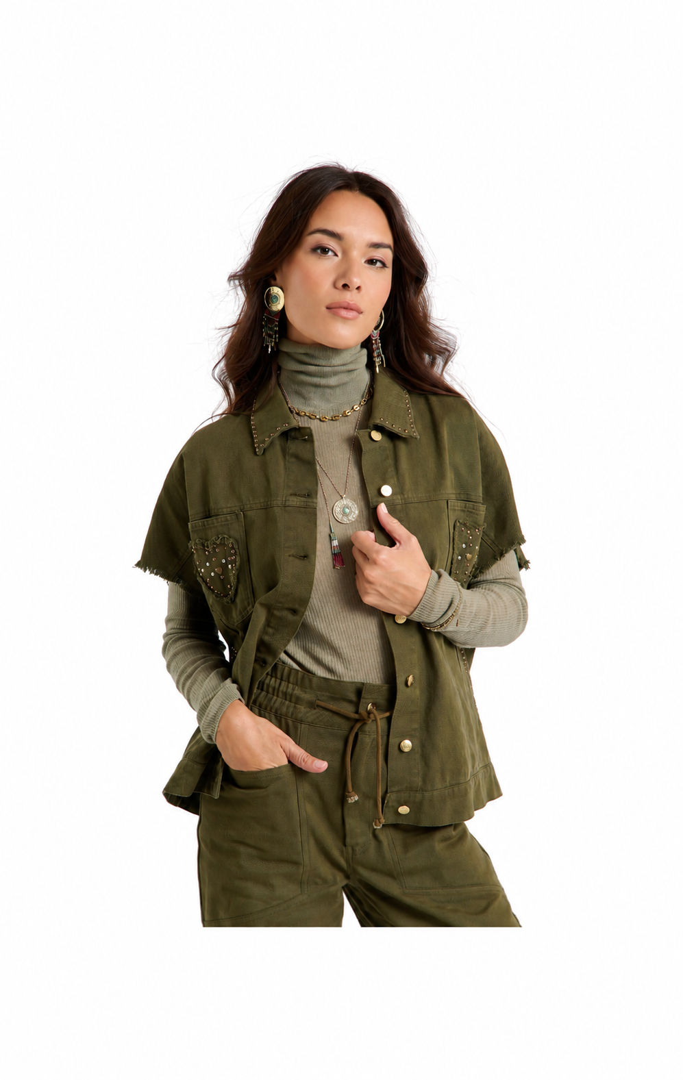 A woman modeling an olive green cropped utility jacket with frayed edges, button details, and decorative studs, worn over a taupe turtleneck and matching olive pants against a plain white background.