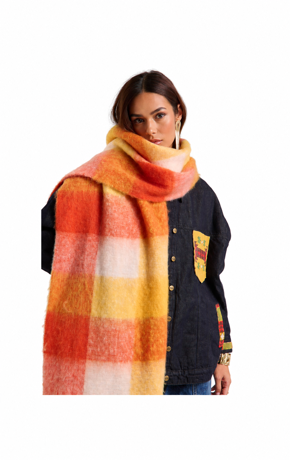 A model wearing a thick, fuzzy plaid scarf in orange, yellow, and white, styled over a dark denim jacket against a plain white background.
