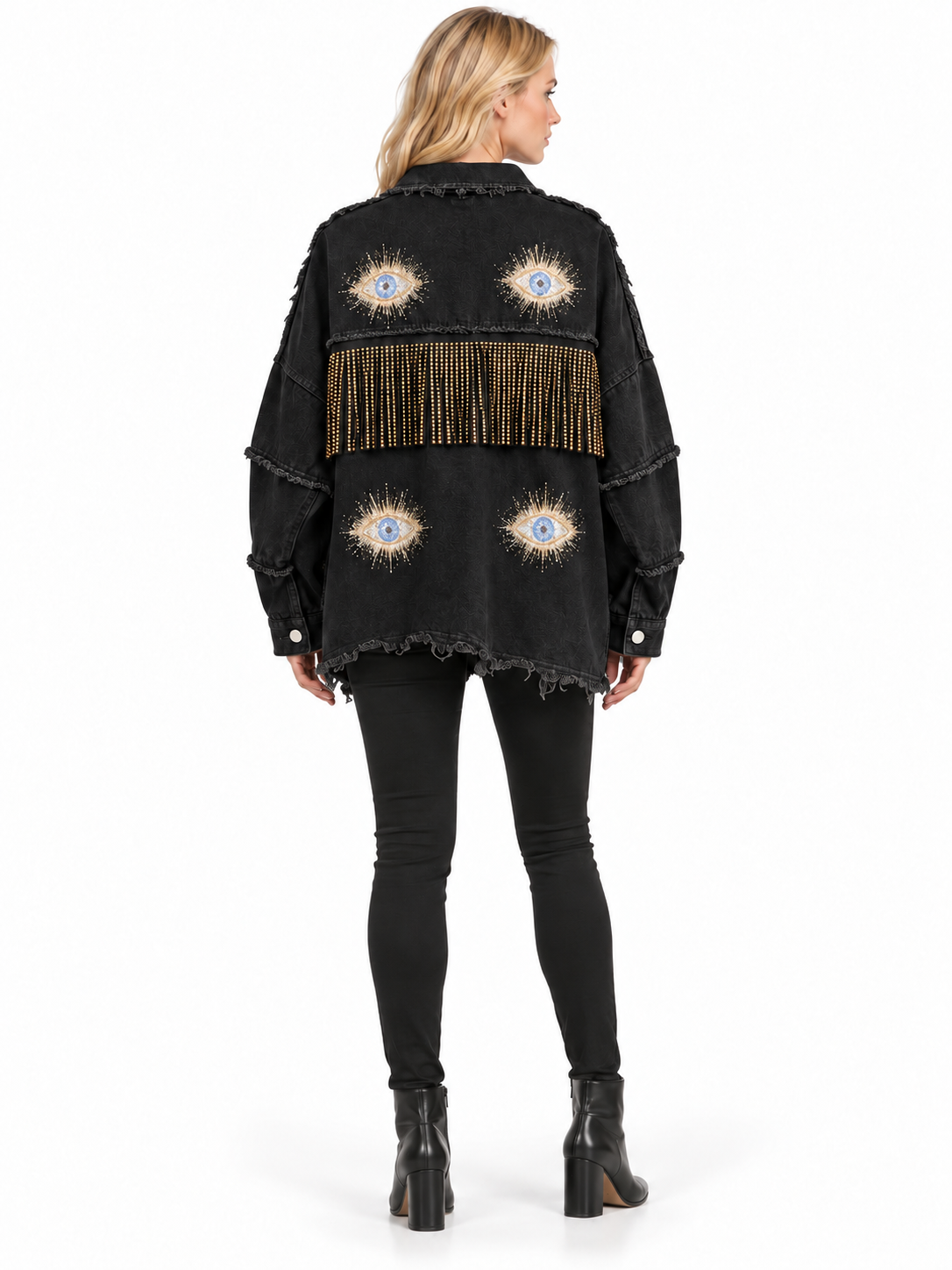 A woman shown from the back wearing a black fringed denim jacket with embroidered eye motifs, paired with black leggings and black ankle boots, on a white studio background.
