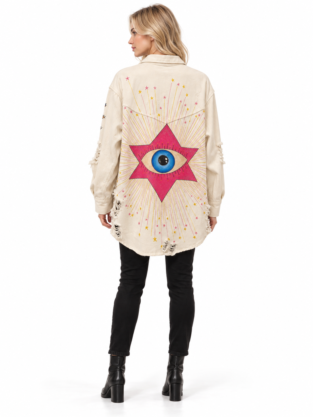 A woman shown from the back wearing a cream-colored distressed denim jacket with a large pink star and blue eye graphic on the back, paired with black pants and black boots, against a white background.