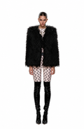 A model stands against a white studio background wearing a voluminous black shaggy faux-fur vest over a beige and black patterned top and shorts, paired with shiny black knee-high boots.