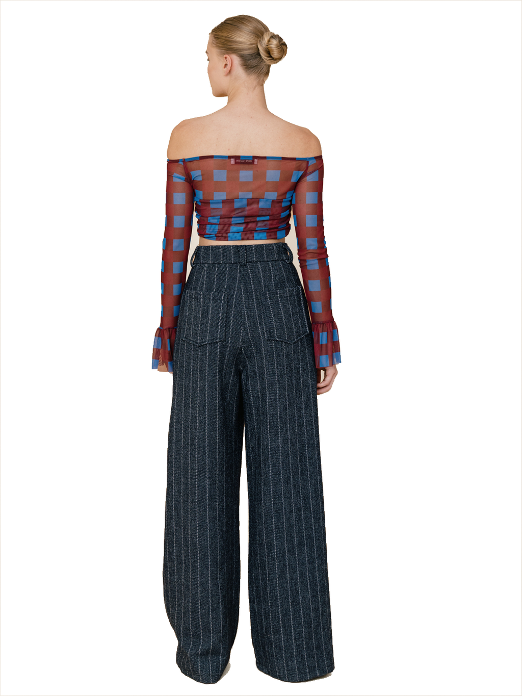 A woman shown from the back wearing a sheer off-the-shoulder long-sleeve crop top with a red and blue check pattern, paired with dark pinstripe wide-leg trousers, against a plain white background.