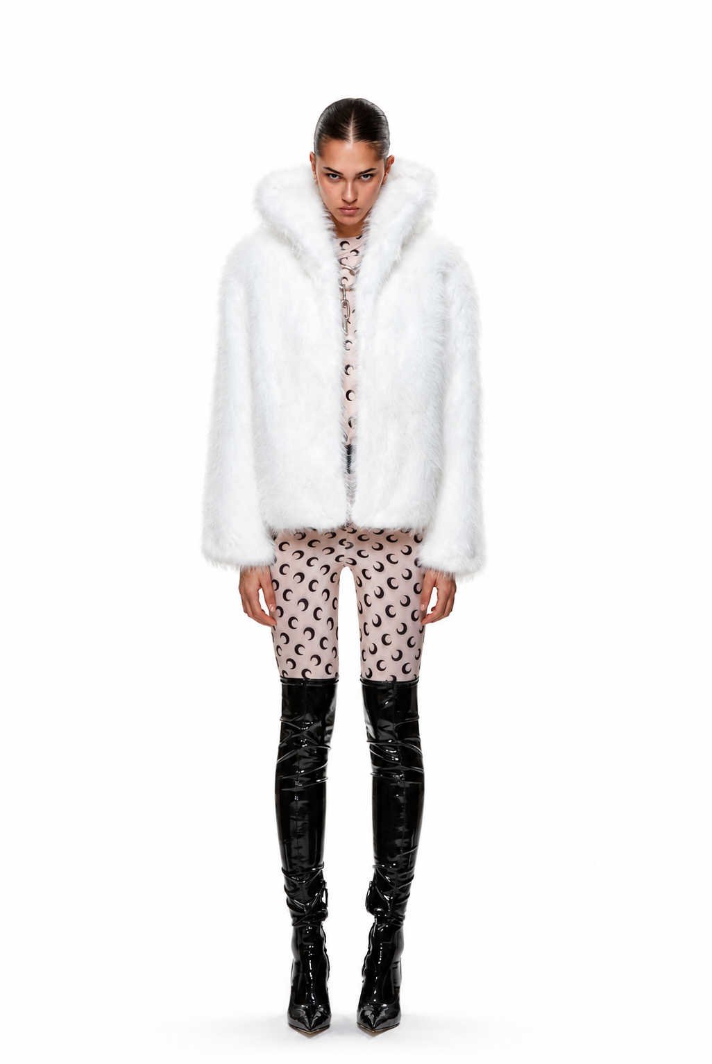 A model stands against a white studio background wearing a voluminous white faux-fur jacket with a large collar, paired with patterned pink and black cropped pants and glossy black over-the-knee boots.