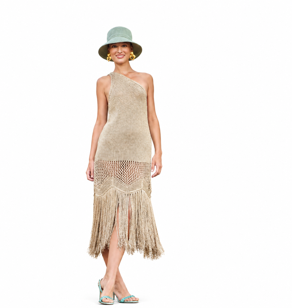 A woman modeling a one-shoulder beige flapper-style dress with fringe detailing, paired with a green bucket hat and turquoise heels, against a plain white background.
