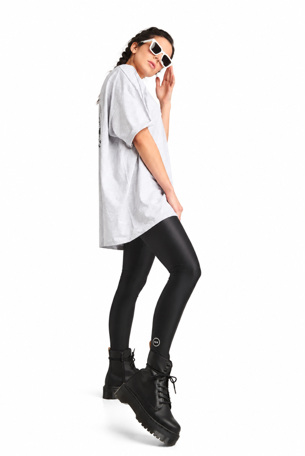A model posing in a white oversized t-shirt, black leggings, and black platform combat boots against a solid white background.