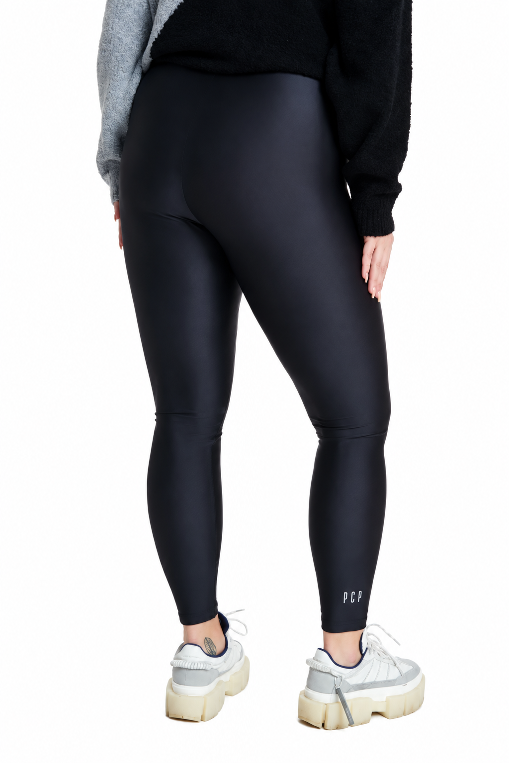 A person shown from the back wearing black high-waisted leggings, a black fuzzy sweater, and white platform sneakers against a plain white studio background.