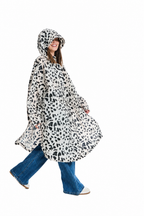 A woman wearing a hooded poncho with a black and white animal print pattern, styled with blue jeans and white sneakers, captured against a solid white background.