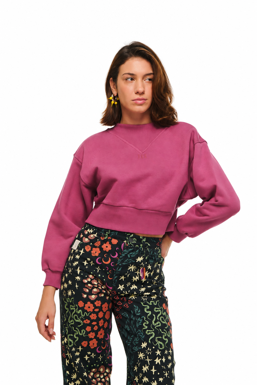 A woman modeling a dusty rose cropped sweatshirt paired with black pants featuring a colorful floral and celestial print, set against a plain white background.