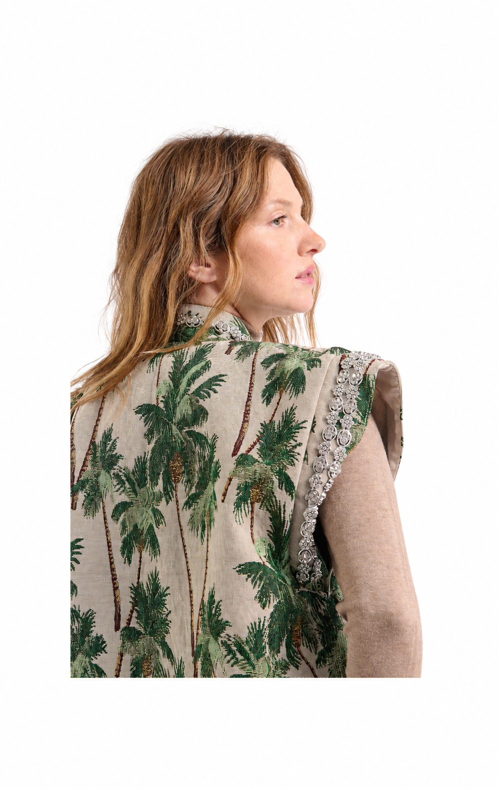 A woman shown from the back wearing a sleeveless beige vest with a green palm tree print and a sheer beige underlayer, set against a plain white background.