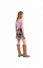 A woman shown from the back wearing a light pink long-sleeve top, a multicolor plaid mini skirt, and tan knee-high boots, photographed against a plain white background.