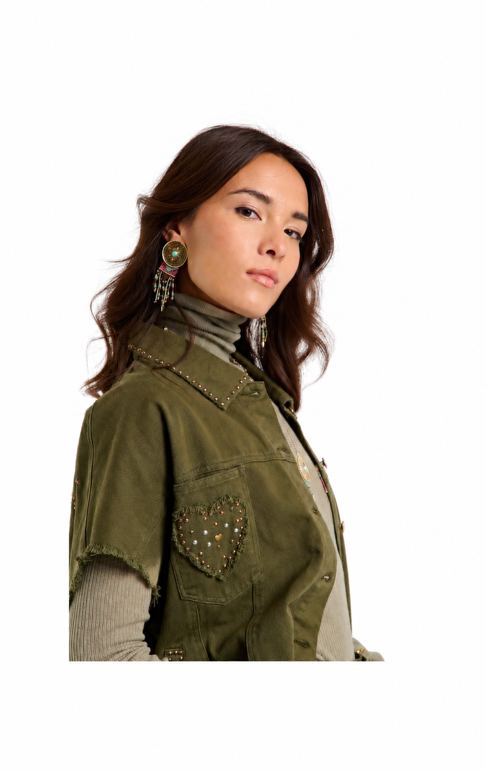 A woman wearing an olive green sleeveless vest with a heart-shaped beaded pocket detail, styled over a beige turtleneck and striped long-sleeve shirt, against a plain white background.
