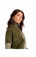 A woman wearing an olive green sleeveless vest with a heart-shaped beaded pocket detail, styled over a beige turtleneck and striped long-sleeve shirt, against a plain white background.
