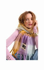 A woman wearing a soft, multicolor striped scarf with fringe, styled over a pink top and blue jeans against a plain white background.