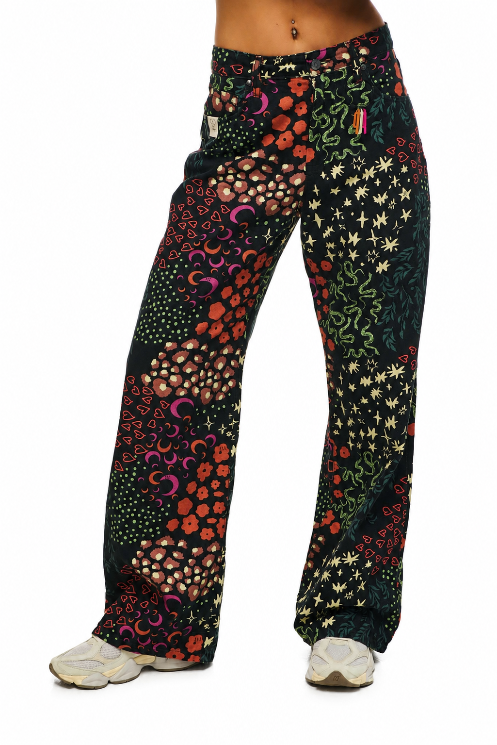 A person wearing loose, wide-leg pants with a dense multicolor abstract print on a black base, paired with white sneakers, shown against a plain white background.