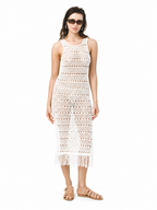A woman modeling a sleeveless white crochet midi dress with fringe at the hem, paired with tan sandals and sunglasses, against a plain white background.