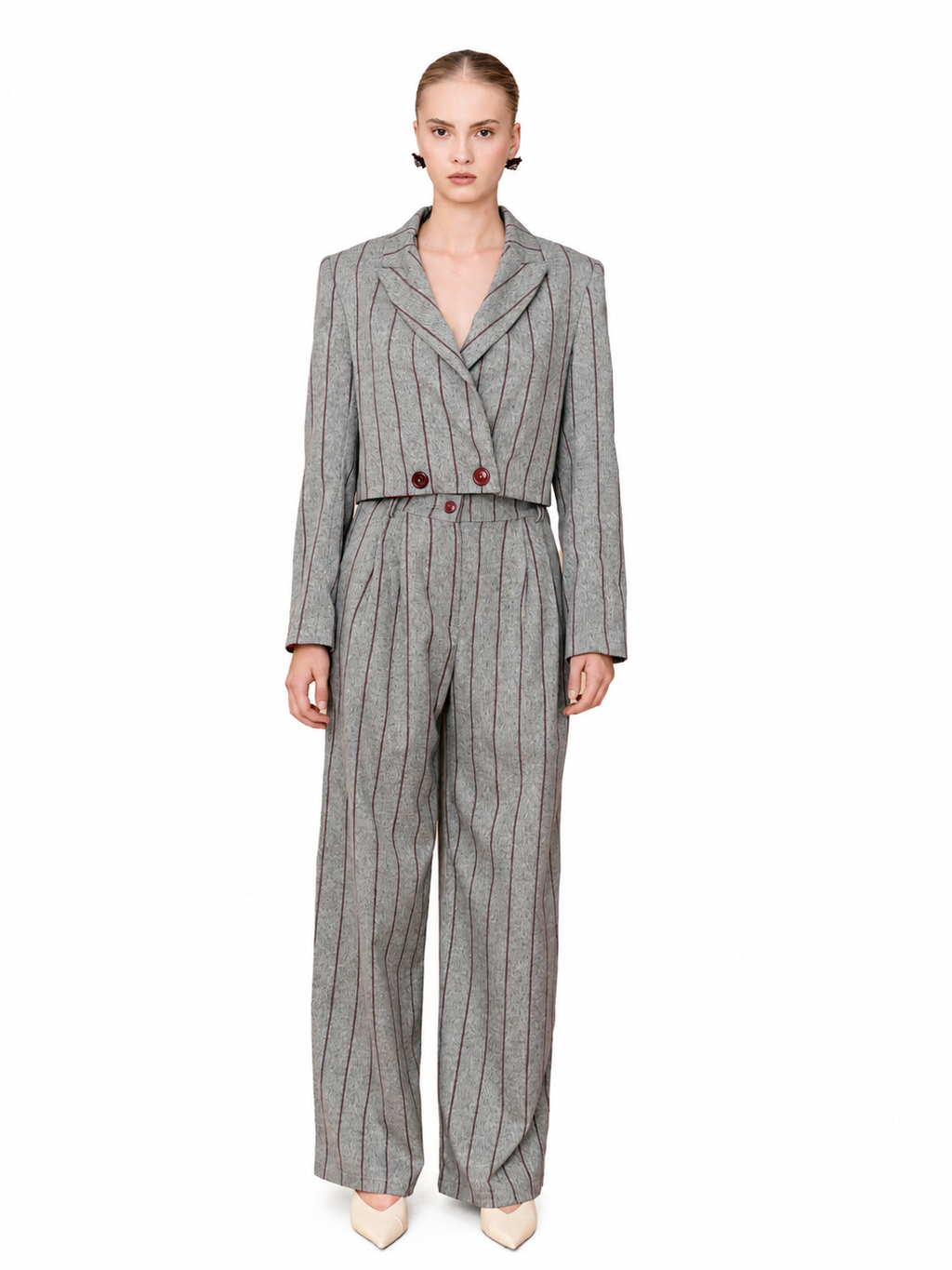 A model wearing a gray pinstripe double-breasted jumpsuit with wide-leg trousers, styled with beige pointed-toe heels against a plain white background.