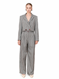 A model wearing a gray pinstripe double-breasted jumpsuit with wide-leg trousers, styled with beige pointed-toe heels against a plain white background.